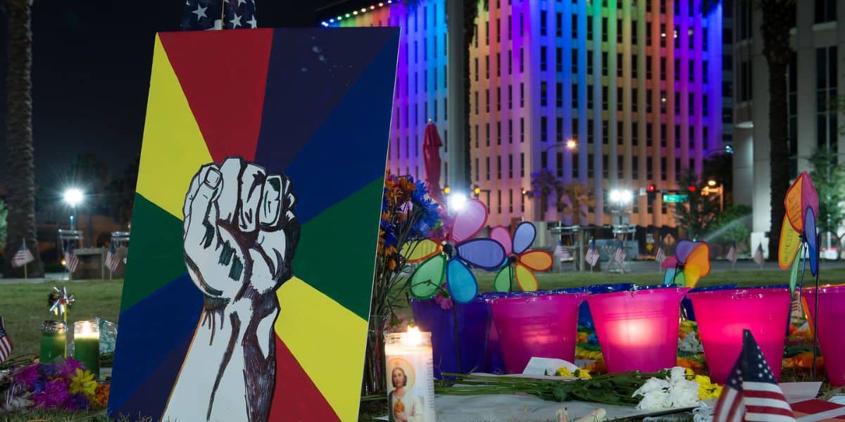 A rainbow fist mural shines at a candlelit Pulse memorial, with Disney World's glowing facade somber in the background.