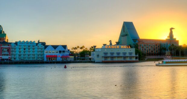 EPCOT’s World Showcase lagoon at sunset, with lively pavilions, a bustling dance hall, and whimsical themed hotels aglow.