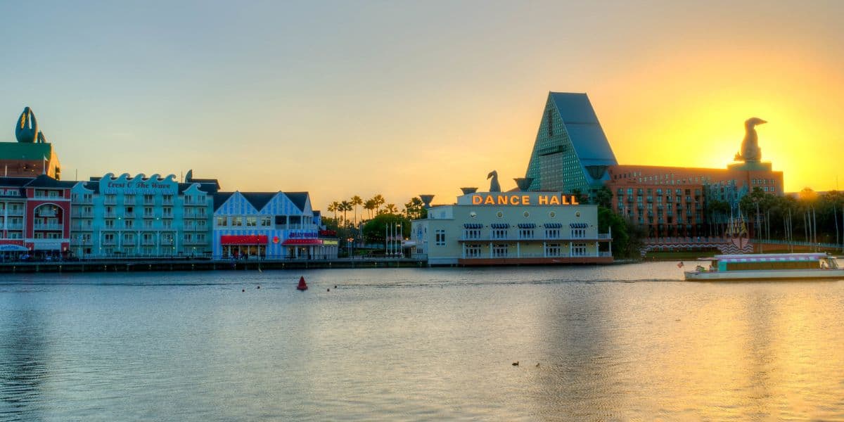 EPCOT’s World Showcase lagoon at sunset, with lively pavilions, a bustling dance hall, and whimsical themed hotels aglow.