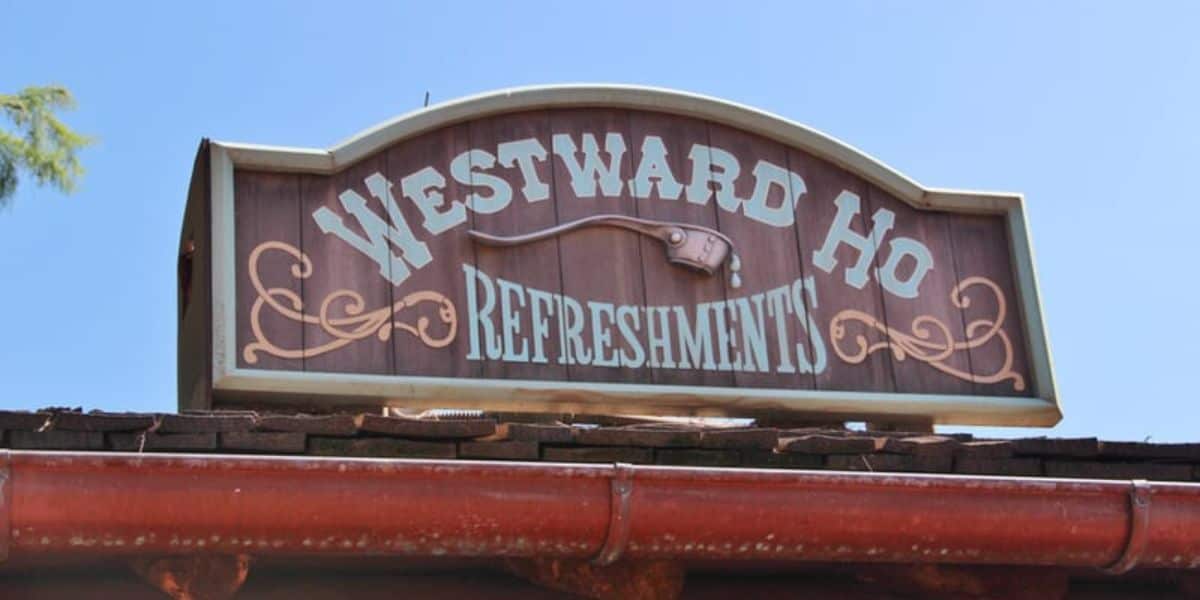 The “Westward Ho Refreshments” sign welcomes guests under a bright blue sky in Frontierland at Magic Kingdom.