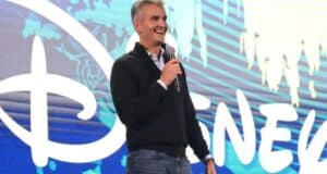 A host with a microphone takes the stage before a giant Disney logo, exciting fans at a Disney entertainment event.