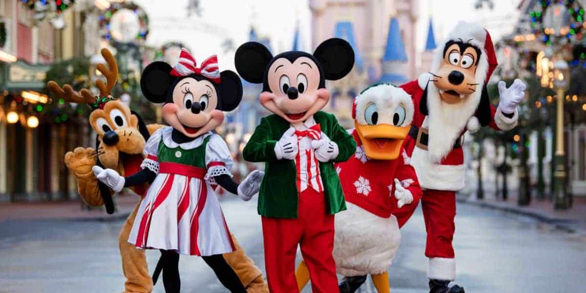 Mickey, Minnie, Goofy, Pluto, and Donald Duck in festive holiday attire at Disney World surrounded by cheerful decorations.