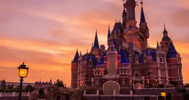 Cinderella Castle illuminated at sunset, sparkling with lights against a vivid orange sky, enchanting Magic Kingdom guests.