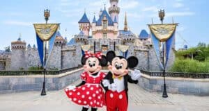 Mickey and Minnie Mouse greet guests in front of Disneyland’s iconic pink castle, adorned with sparkling blue rooftops and shimmering gold banners.