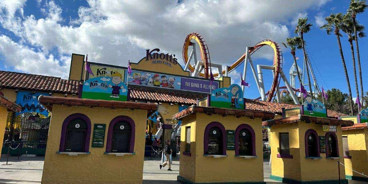 Knott’s Berry Farm’s iconic yellow ticket booths stand welcoming guests at the entrance, with a thrilling roller coaster set against the sky—an energetic scene that captures the anticipation for Teen Takeover or Beach Riot festivities.