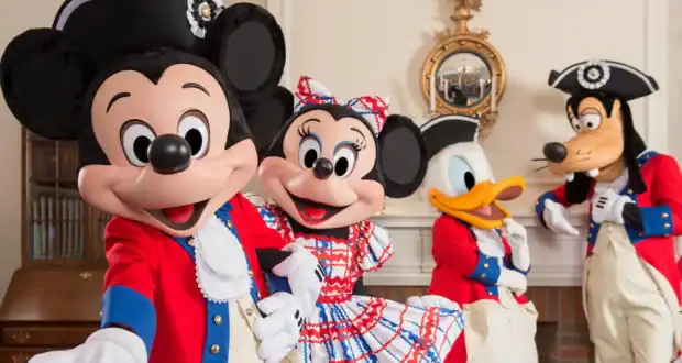 Mickey, Minnie, Donald, and Goofy greet guests in patriotic colonial outfits at a lively indoor Disney Parks celebration.