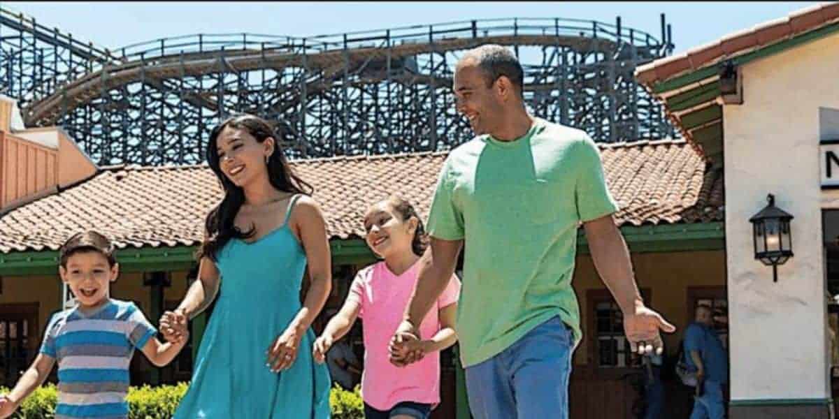 A cheerful family of four strolls together in the sunshine near GhostRider’s towering wooden tracks at Knott’s Berry Farm.
