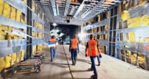 A team of workers in bright safety vests explore a behind-the-scenes tunnel under construction, revealing the unfinished magic beneath the theme park with its exposed walls and ceiling.