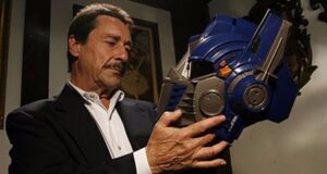 A sharply dressed guest pauses at Universal Studios, thoughtfully admiring the iconic blue Optimus Prime helmet from Transformers, evoking the feeling of stepping into a blockbuster movie moment.