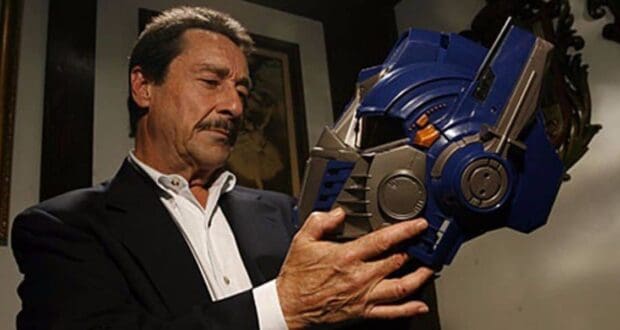 A sharply dressed guest pauses at Universal Studios, thoughtfully admiring the iconic blue Optimus Prime helmet from Transformers, evoking the feeling of stepping into a blockbuster movie moment.