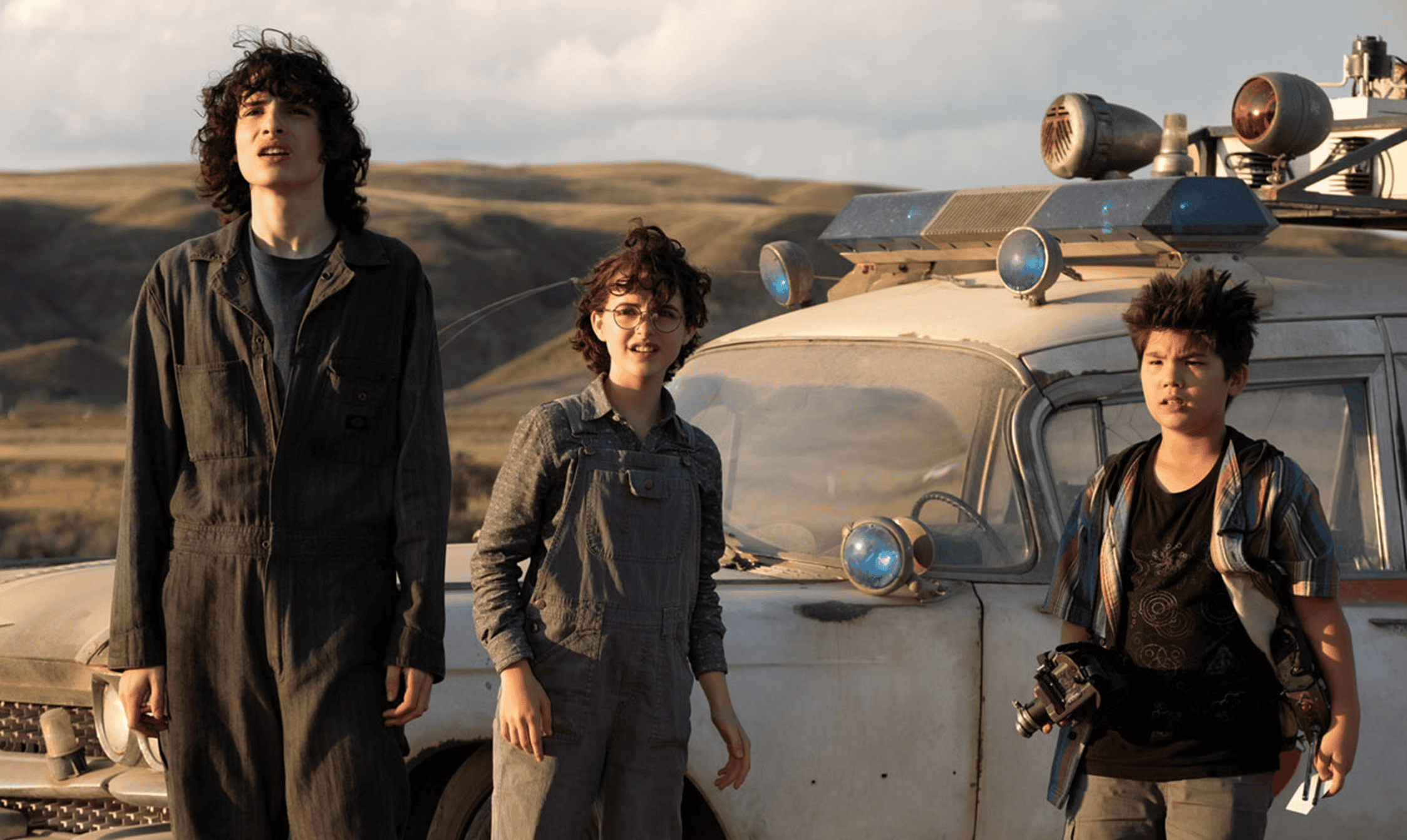 Aerial shot of three diverse young filmmakers standing in front of a vintage vehicle on a remote, hilly landscape showcasing creative film production at DIVO Post Production.
