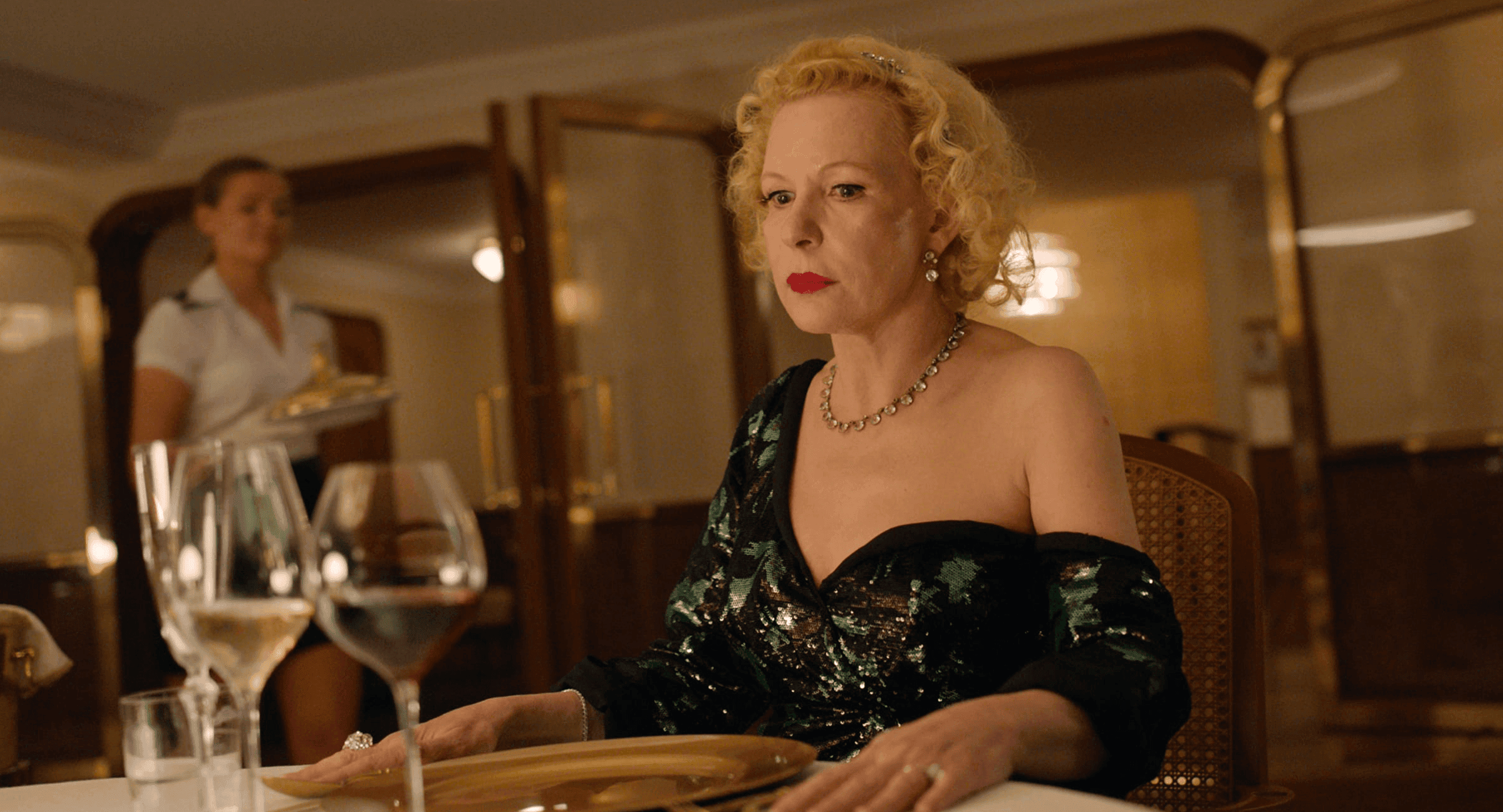 Elegant woman in glamorous black dress seated at a dining table with wine glasses, in a luxurious restaurant setting, captured during production at DIVO Post Production.