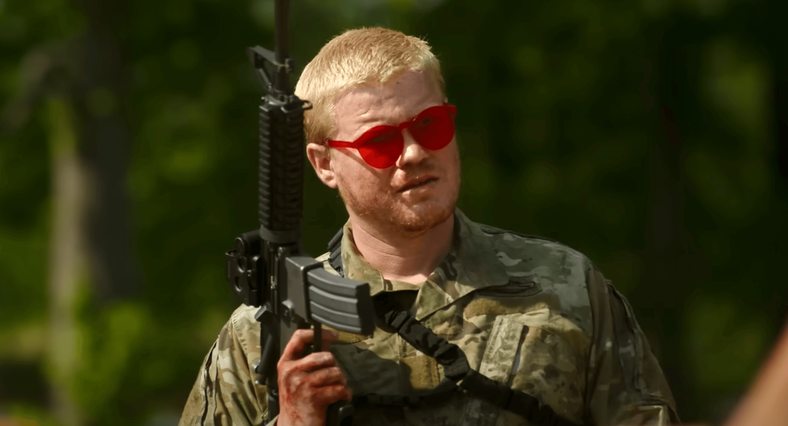 Military soldier holding assault rifle during outdoor training, wearing camouflage uniform and red sunglasses, emphasizing tactical operations and military gear.