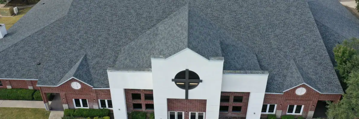Front-facing aerial image of church with contemporary gray asphalt shingle roof and brick facade, showcasing church roof replacement San Antonio by Dolan Roofing & Construction
