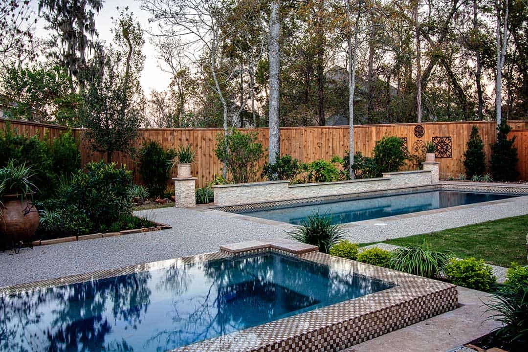 Beautiful backyard pool area in Sugar Land featuring a modern design, surrounded by greenery and a wooden privacy fence, perfect for relaxing and entertaining.