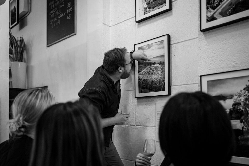 Man examines photo in art gallery, holding wine.
