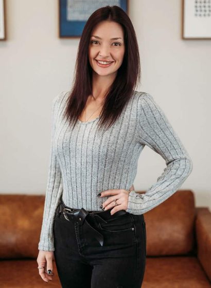 Smiling woman in gray sweater standing indoors.