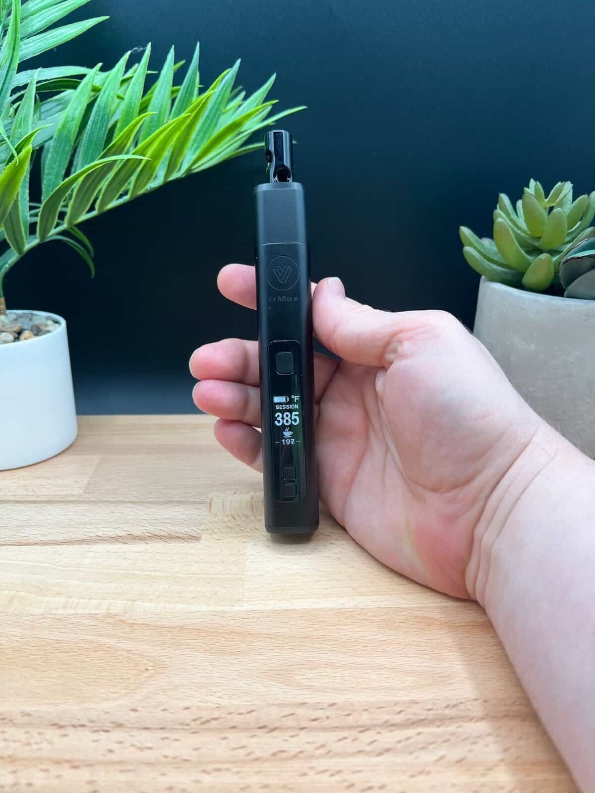 Here’s how you can optimize your image for SEO and engagement: SEO Alt Text (For Search Engines) "XMAX V3 Pro dry herb vaporizer held in hand, displaying 38.5W power settings with a sleek black design, set against a wooden surface and green plants. Ideal for showcasing vaping technology and aesthetics.