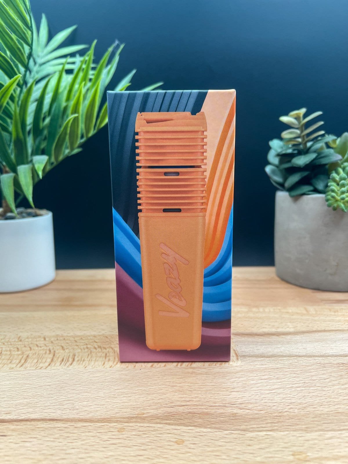 Boxed Storz & Bickel Veazy vaporizer in orange with packaging displayed on a wooden surface — featured in our Veazy Review.