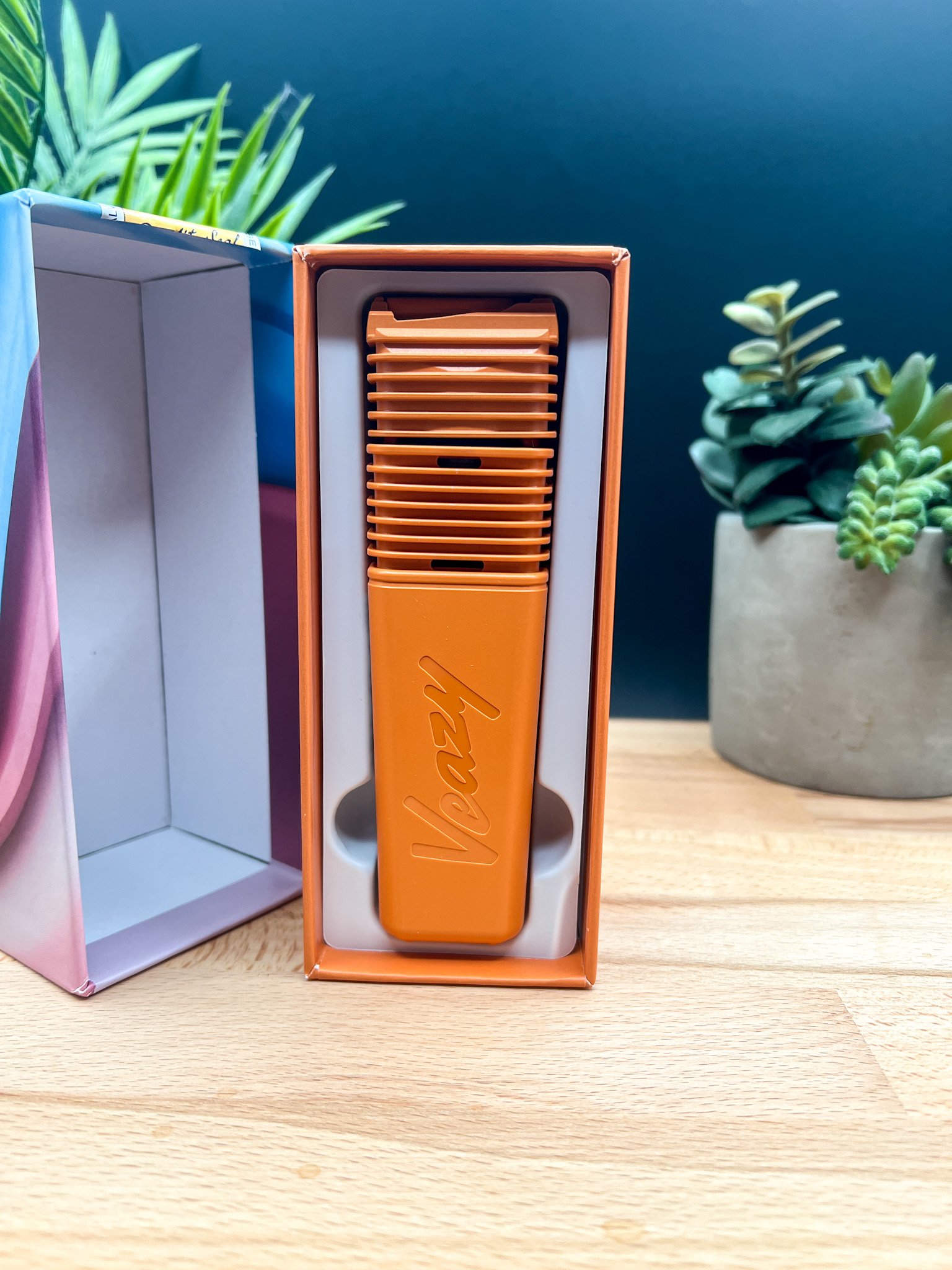 Orange Storz & Bickel Veazy vaporizer displayed inside its box with ribbed design and angled mouthpiece — featured in our Veazy Review.