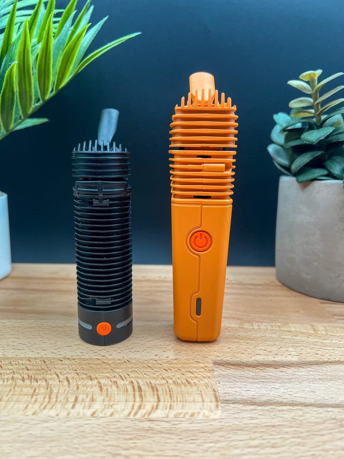 Crafty+ vaporizer next to the orange Storz & Bickel Veazy on a wooden surface with plants — featured in our Veazy Review.