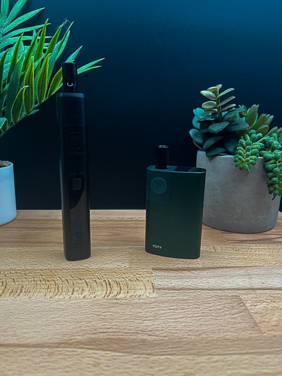 POTV Lobo and XMAX V3 Pro dry herb vaporizers side‑by‑side on a wood surface with plants in the background, showing design and size differences