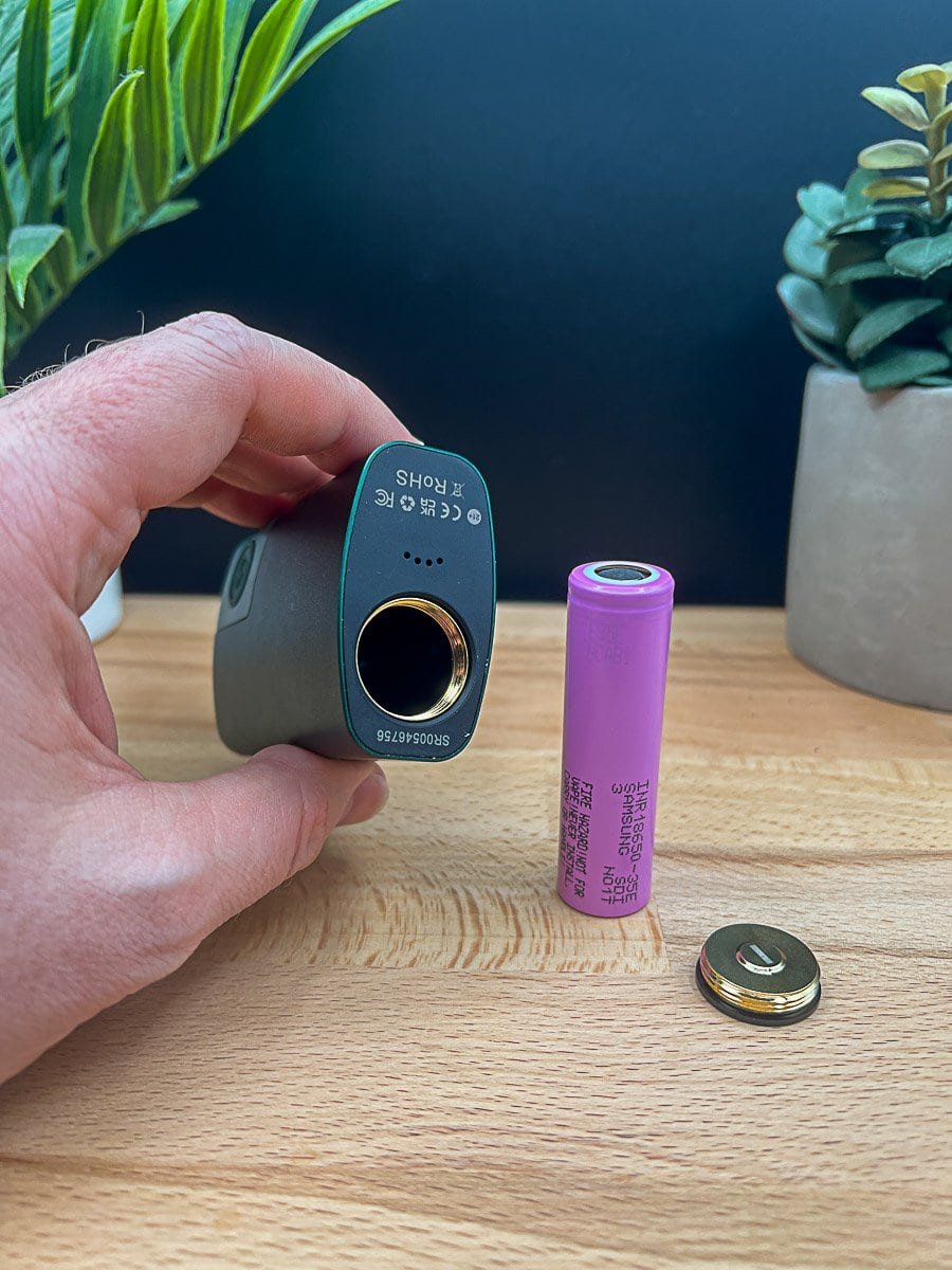 This photo showcases a close-up of the POTV Lobo vaporizer’s black mouthpiece held in hand, revealing the internal mesh filter and sleek contours. The green body of the device sits blurred in the background atop a wooden surface, accompanied by two potted plants for a natural, lifestyle-oriented setting. As covered in our POTV Lobo Review 2025, this image illustrates the modular design and attention to airflow engineering found in the Lobo's updated build.