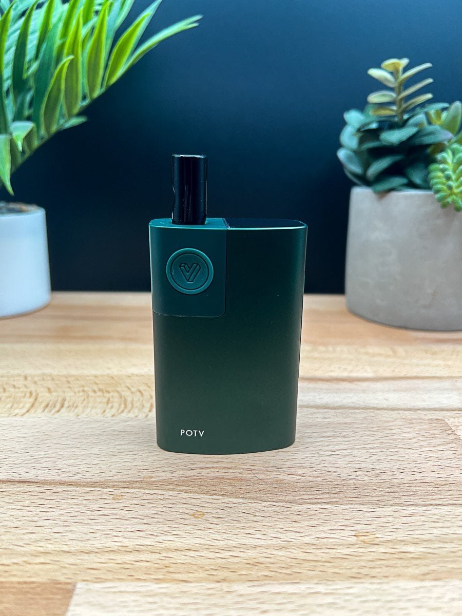 Green dry herb vaporizer by POTV on wood surface with houseplants in background