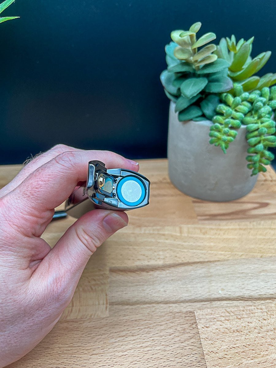 XMAX Starry V4 vaporizer with open mouthpiece revealing ceramic chamber, held over wood surface with succulent plants in background