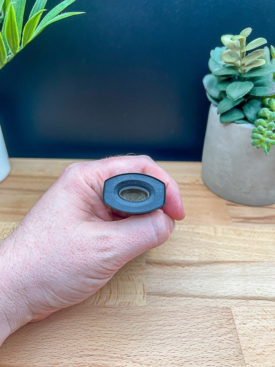 XMAX Starry V4 mouthpiece with metal screen filter held in hand, shown over wood surface with potted plants in background