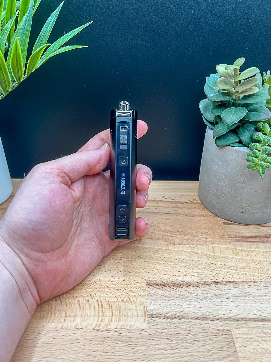XMAX Starry V4 vaporizer review displaying temperature settings on screen, held over wood surface with potted plants in background