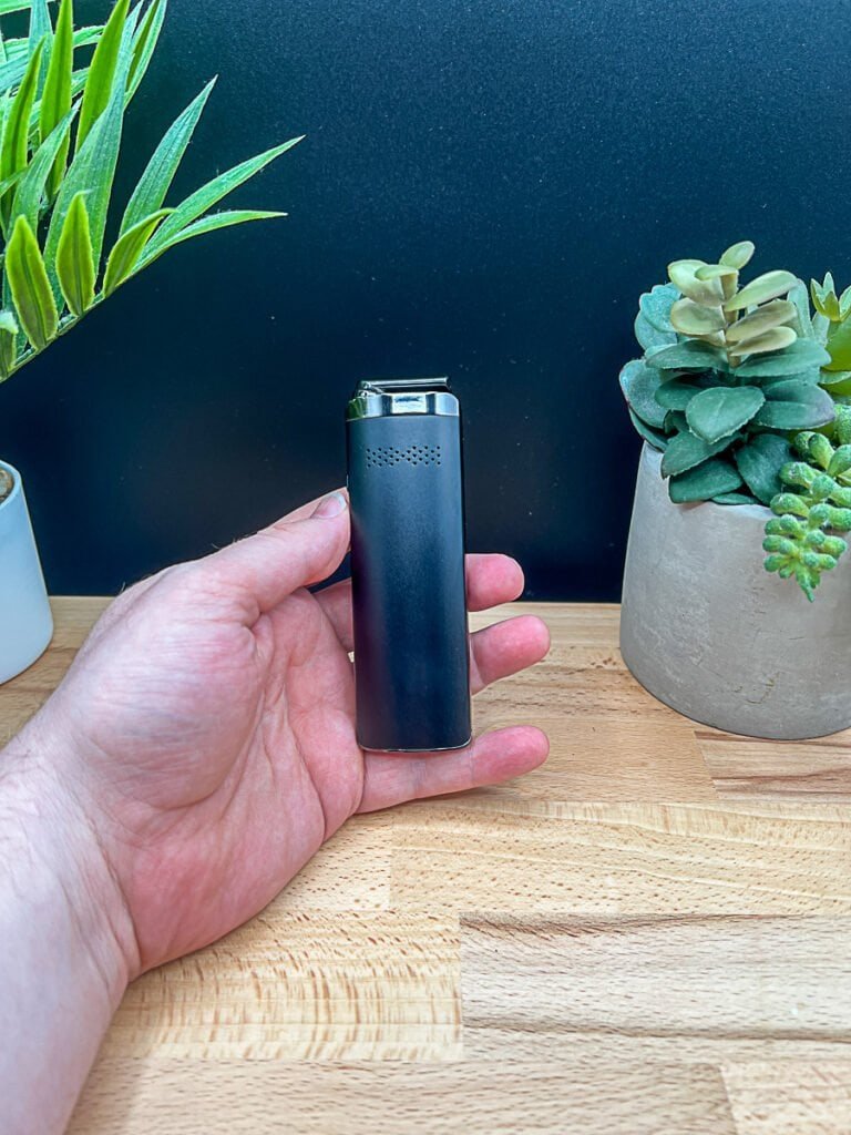 XMAX Starry V4 vaporizer held in hand with potted plants in background