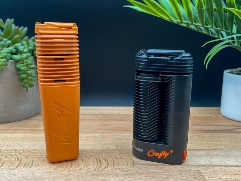 Storz & Bickel Crafty+ and Veazy portable vaporizers side by side on a wooden table with plants in the background.”