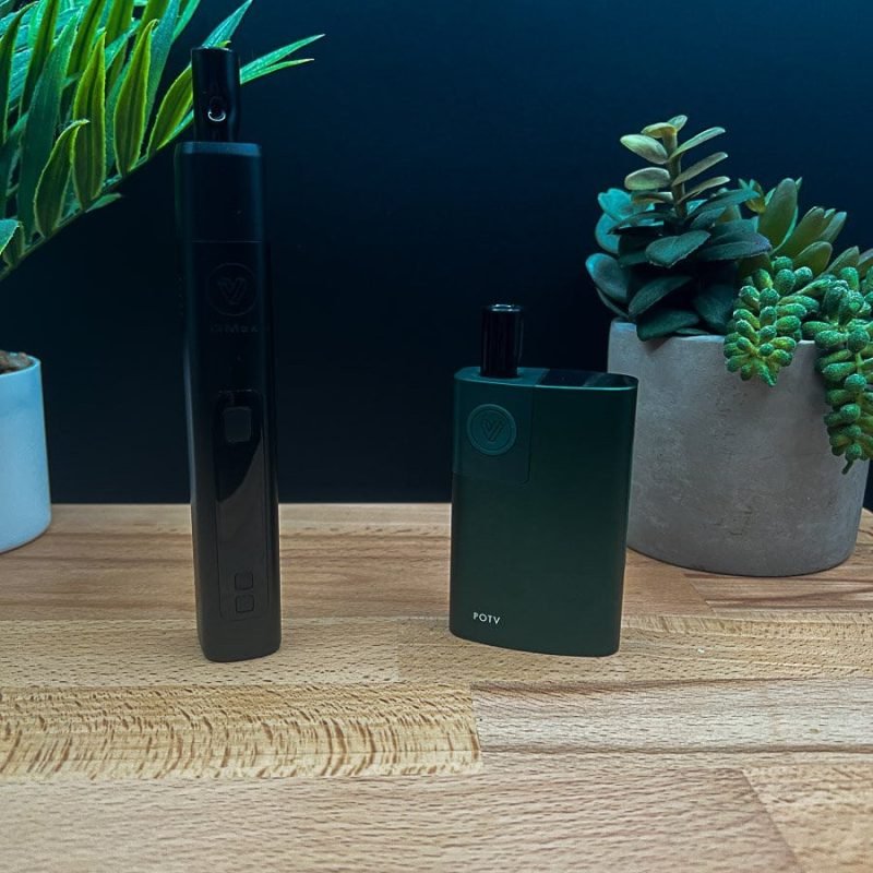 POTV Lobo and XMAX V3 Pro dry herb vaporizers side‑by‑side on a wood surface with plants in the background, showing design and size differences