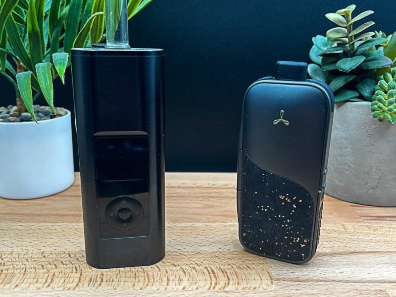 Arizer Solo 3 v2 and AirVape Legacy Pro 2 portable vaporizers side by side on a wooden surface with plants in the background.