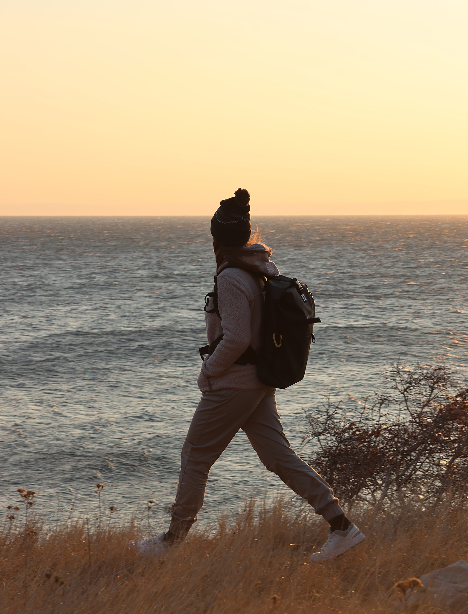 Waterproof backpack being carried by a hiker along the coast at sunset.