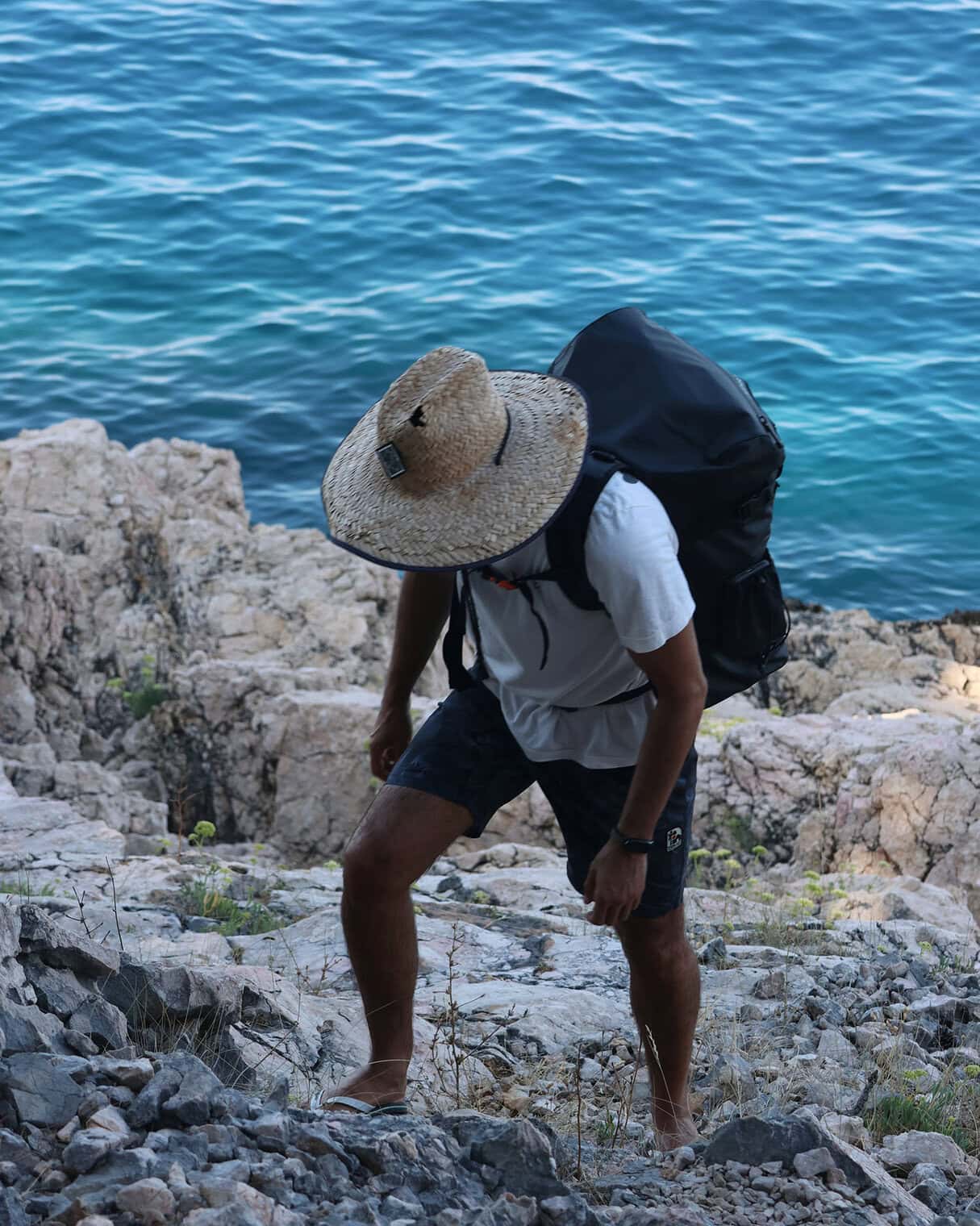 Person with a waterproof travel backpack exploring rocky shoreline by the water.