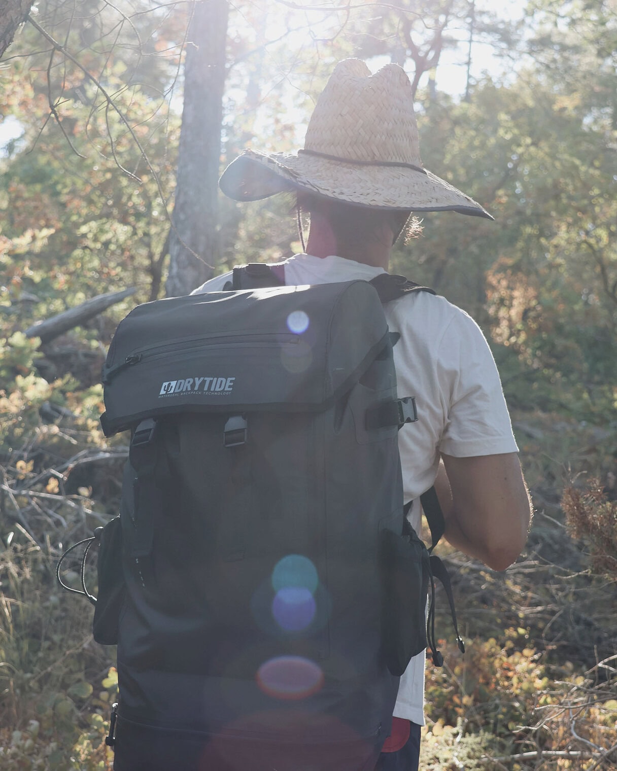 Person with waterproof travel backpack exploring forest in sunlight.