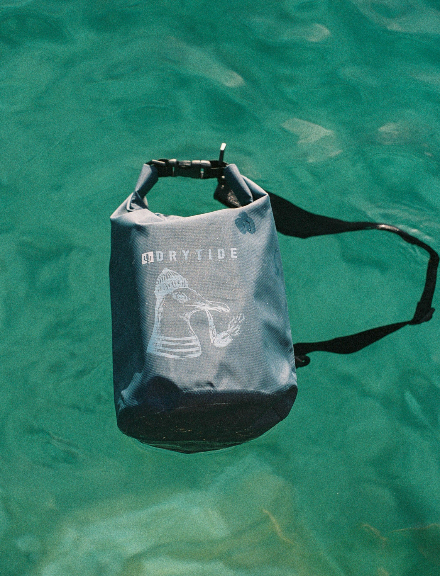 DryTide 5L dry bag Tonga Waterproof dry bag floating on water with drytide logo and strap attachment.