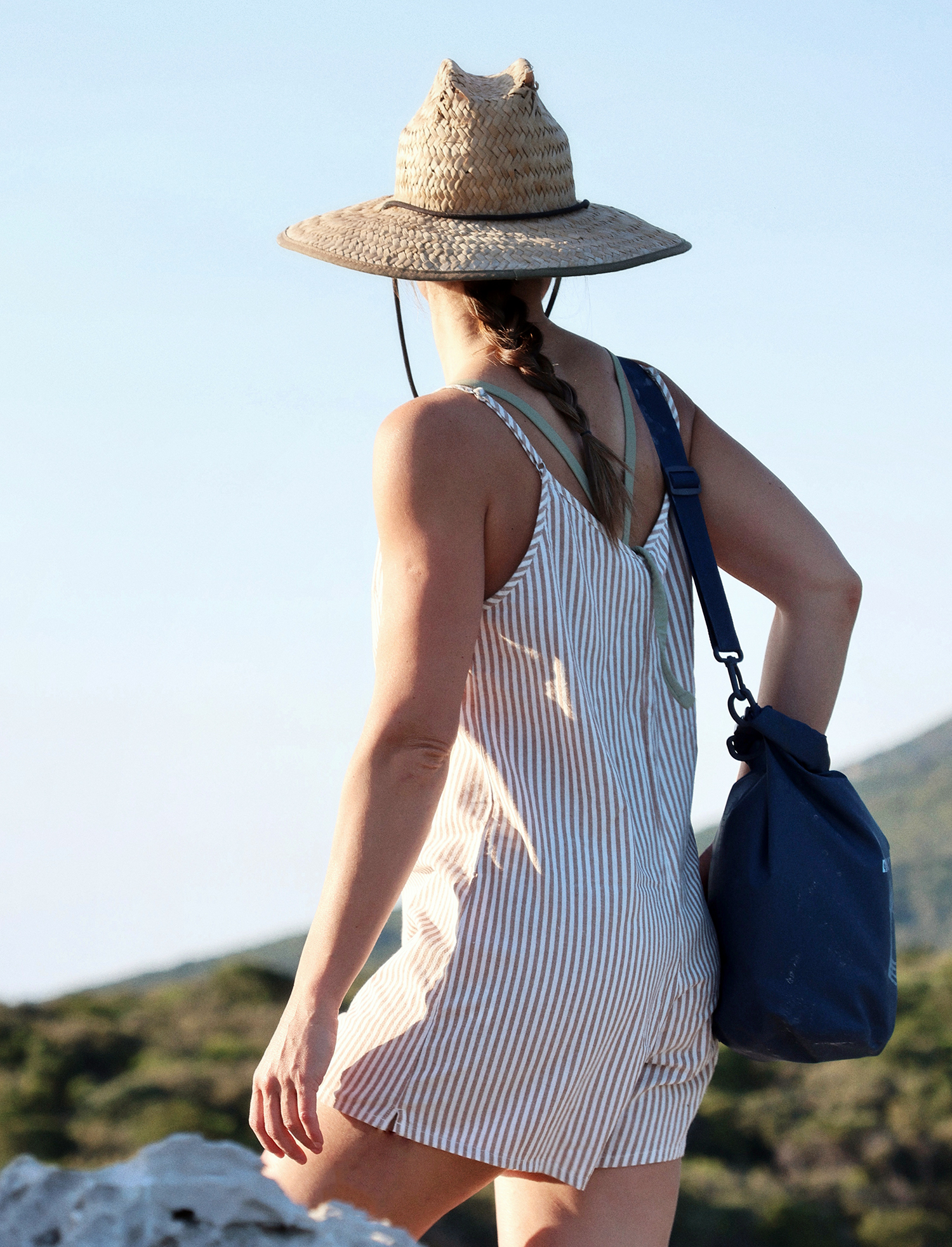 DryTide 5L dry bag shoulder strap Waterproof backpack and sun hat on a woman outdoors in a natural setting.