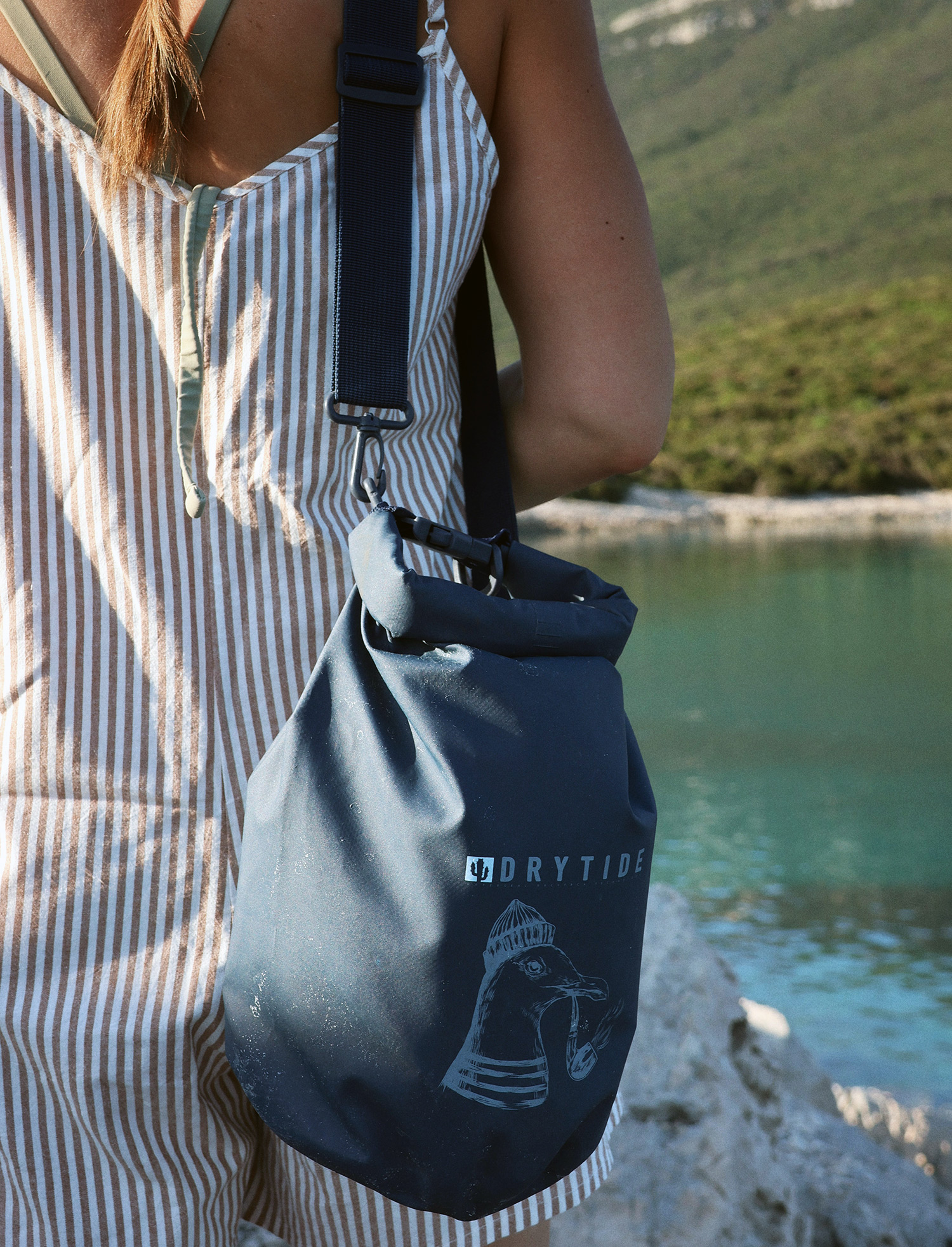 DryTide 5L dry bag summer life Waterproof dry bag with Drytide logo hanging from a person's shoulder near a river.