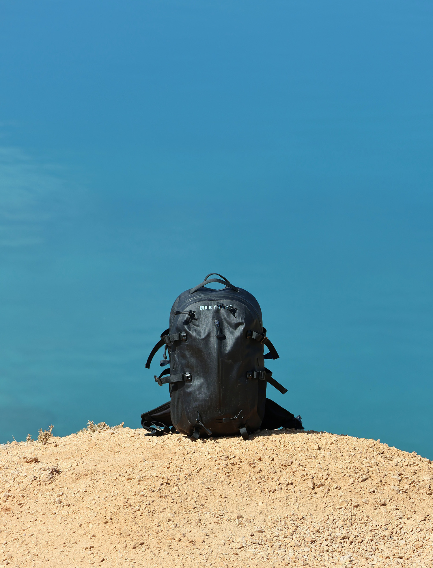 Waterproof backpack on sandy terrain under clear blue sky.