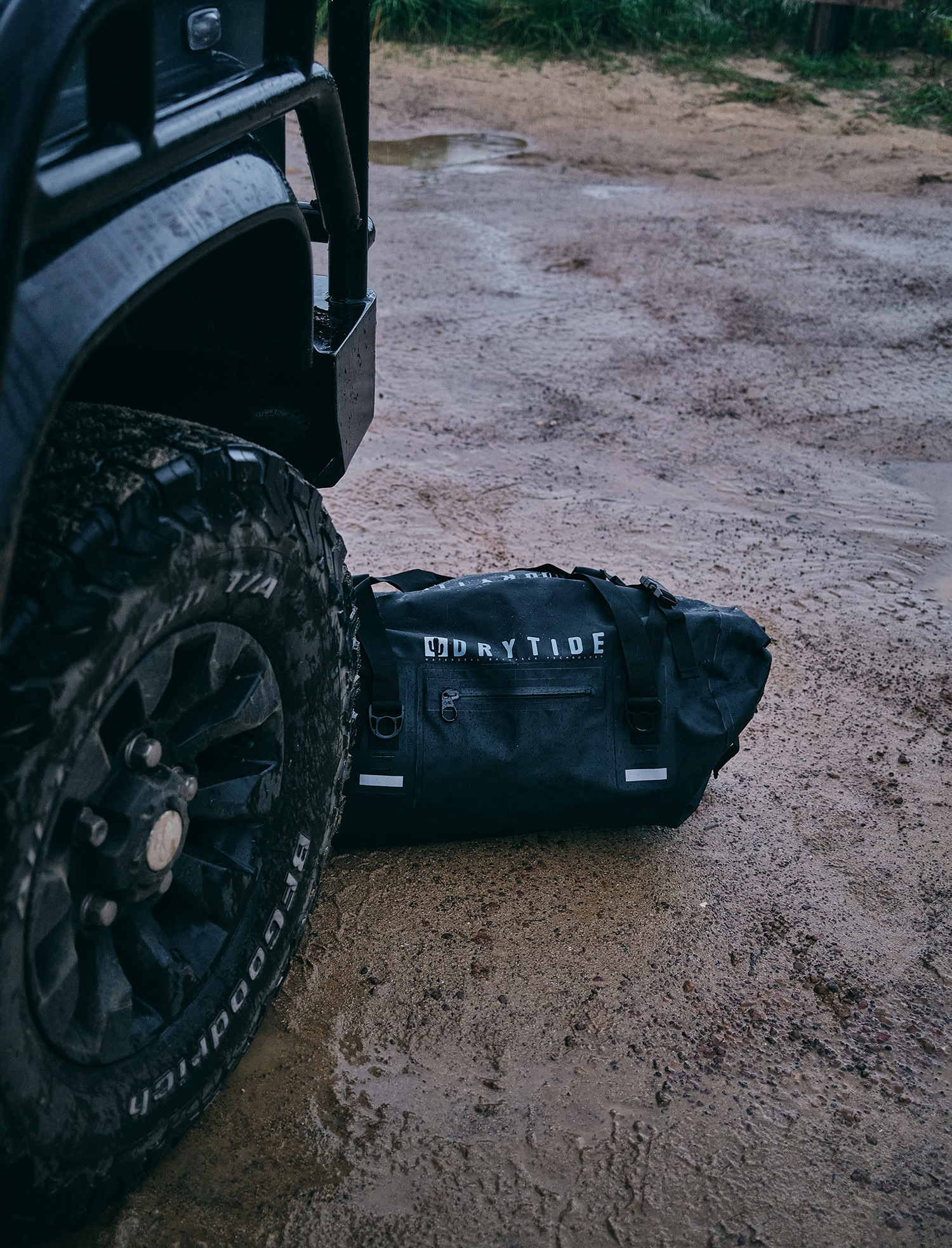 Waterproof dry bag next to off-road vehicle on muddy ground.