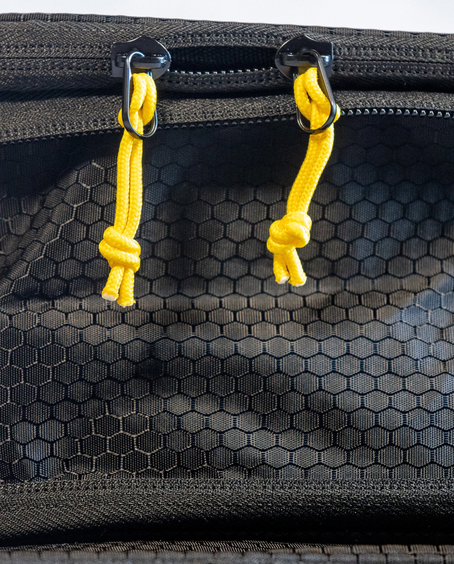 Close-up of waterproof backpack zippers with yellow cords and black fabric.