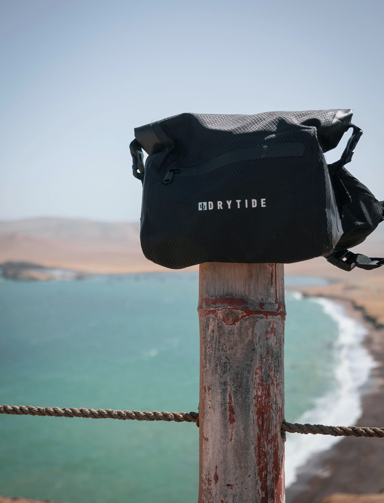 Waterproof dry bag on a wooden post overlooking the ocean coastline.