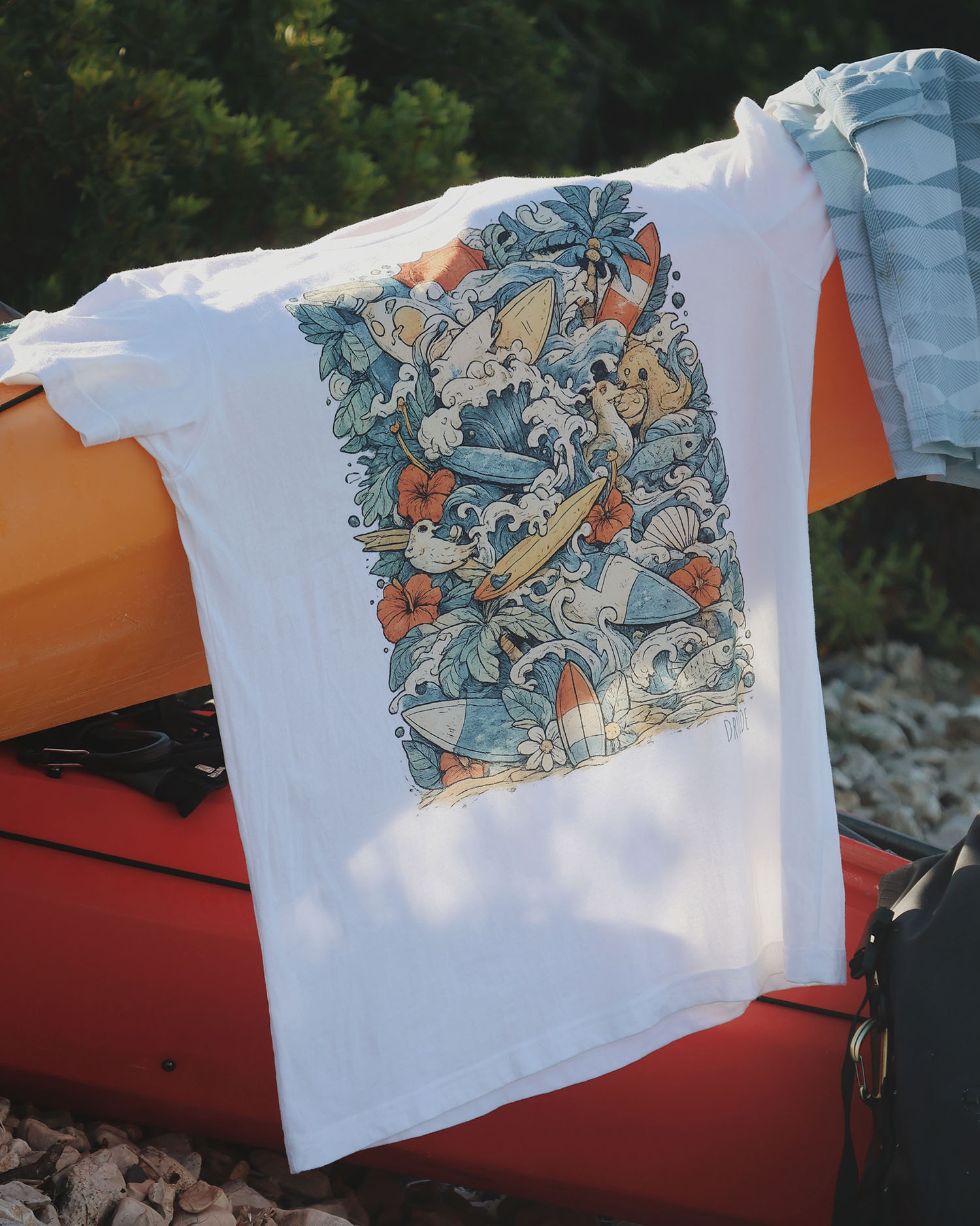 Jungle madness tee drying on sea kayak Jungle-themed graphic T-shirt hanging on kayak with outdoor scenery.
