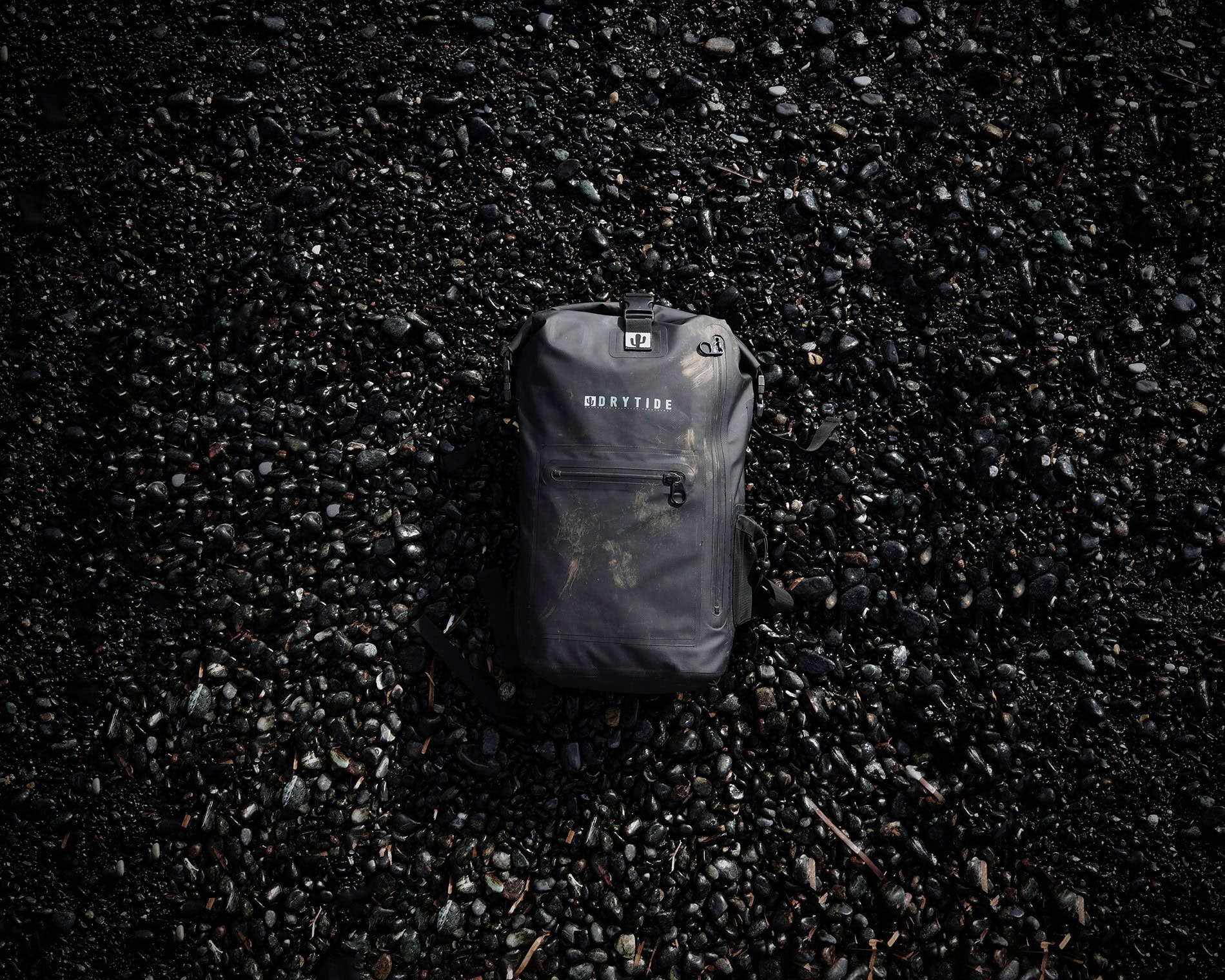 a black waterproof backpack on a black pebble beach