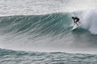 Surfer riding a wave with a waterproof backpack on a sunny day.
