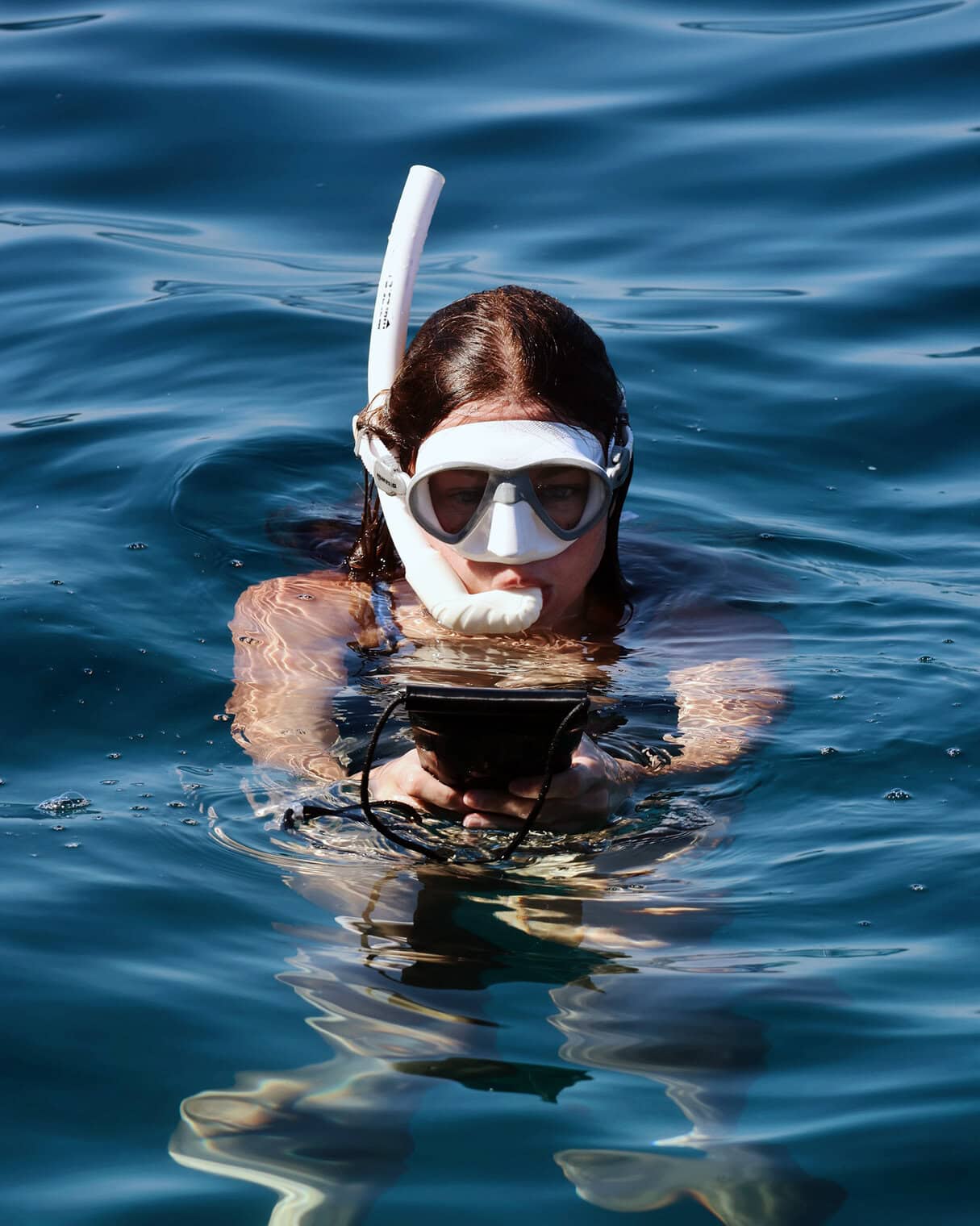 Woman snorkeling with waterproof phone pouch in open water.