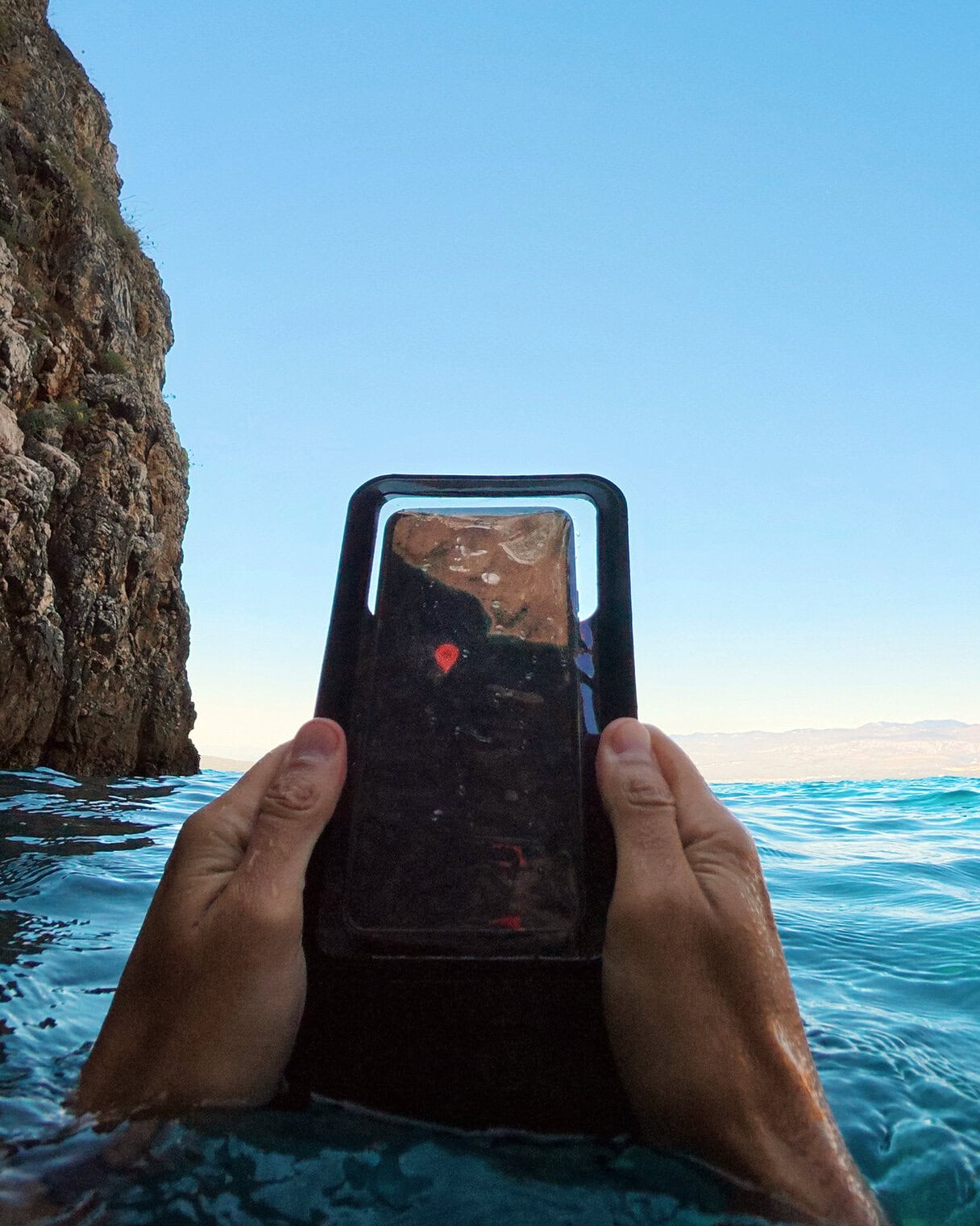 waterproof phone pouch checking the map in the sea Person holding waterproof phone pouch in water near rocky shoreline.
